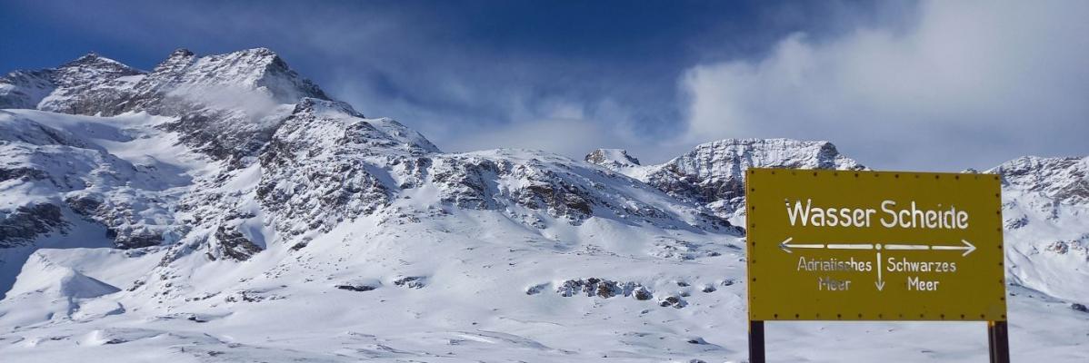 Verschneite Berglandschaft an der Wasserscheide am Berninapass mit Piz Cambrena